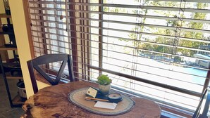 Une table ronde en bois dont le bord est laissé à l’état naturel, une petite plante en pot, un bloc-notes et une bougie posés sur un set de table en fibres tressées.
