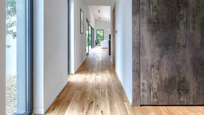 Ein moderner Flur mit Holzboden, weißen Wänden und einem großen Fenster links.