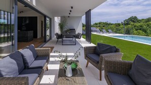 Eine moderne Außenpatio mit Essbereich, Lounge-Stühlen und Blick auf ein Schwimmbad und Grünflächen.