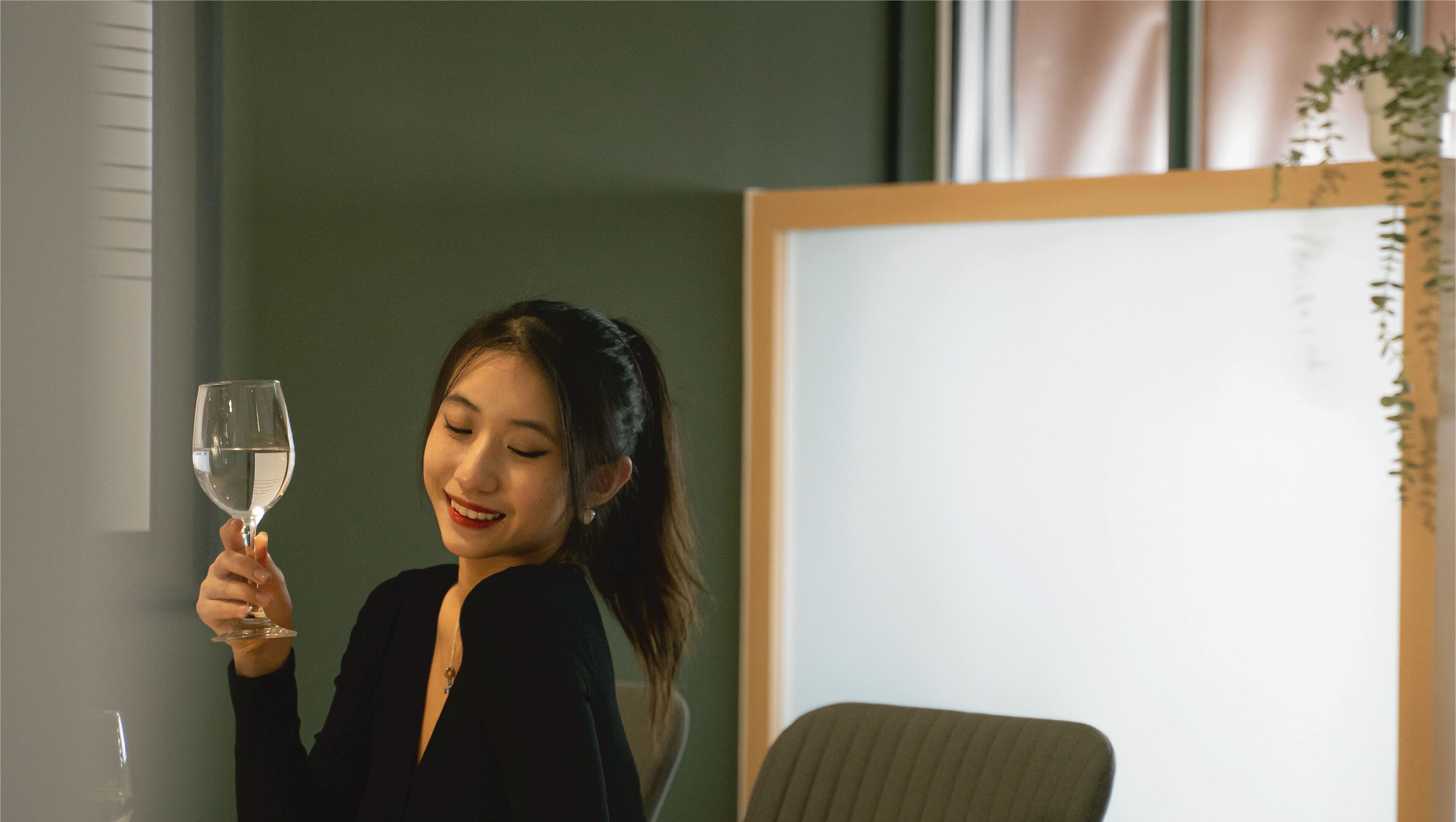 A person holding a wine glass in a room with a green wall and a whiteboard.