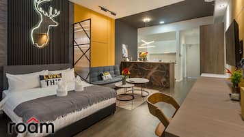 A modern hotel room with a bed, sofa, dining table, and a neon deer sign.