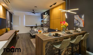 A modern kitchen with a marble island, bar stools, and a dining area with a table set for two. - Chambers Residence Kuala Lumpur by Roam (Kuala Lumpur)