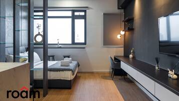 A modern bedroom with a bed, desk, and large window.
