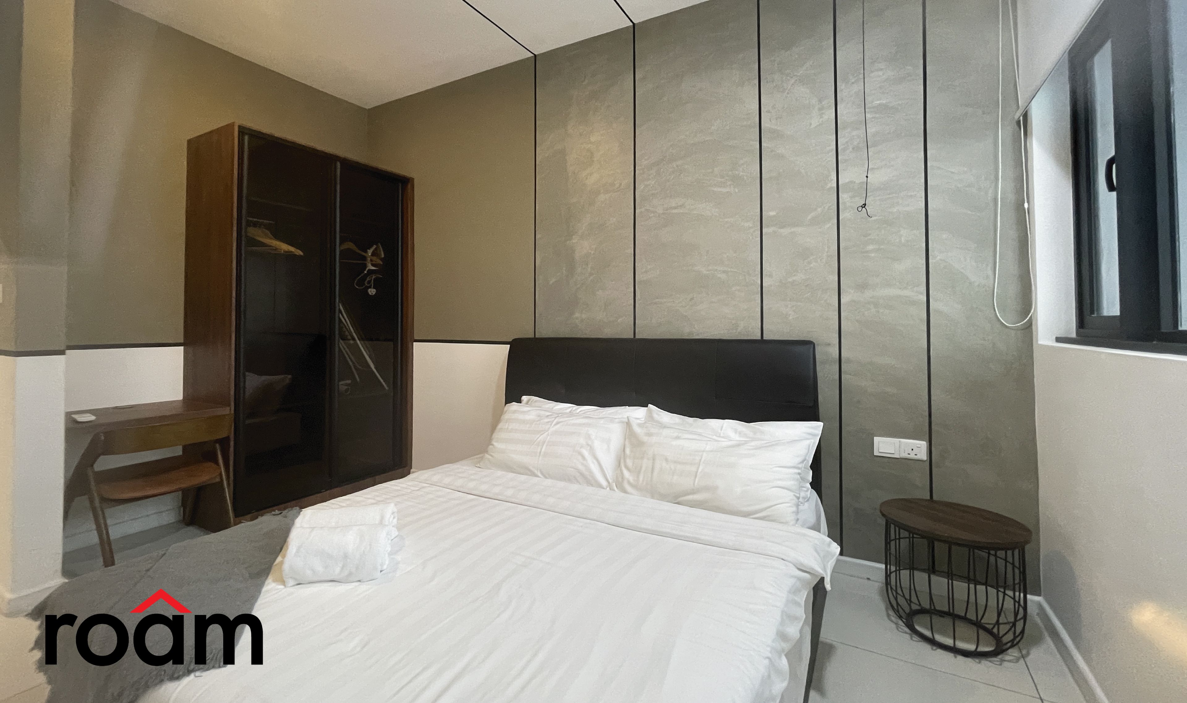 A bedroom with a bed, a wardrobe, a small table, and a window.