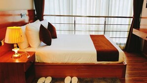 A neatly made bed with a white comforter and a brown throw blanket, a wooden nightstand with a lamp, and a pair of slippers on the floor. - Hotel Thimphu Central (Thimphu)