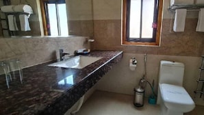 A bathroom with a marble countertop, a toilet, a window, and a towel rack. - Hotel Thimphu Central (Thimphu)
