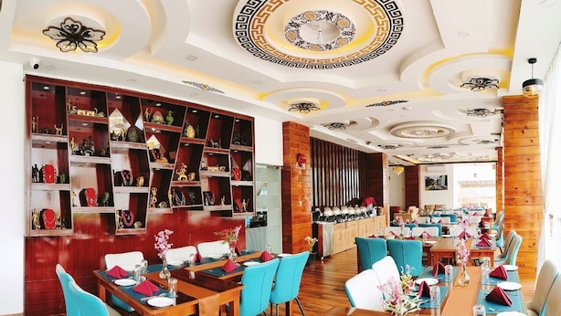 A restaurant with wooden floors, blue chairs, and a long dining table set for multiple guests. - Hotel Thimphu Central (Thimphu)