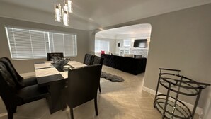 A dining area with a table and chairs, a kitchen in the background, and a metal rack. - Insta-Worthy! Just Remodeled! Private Home! Luxurious & Brand New  (San Bernardino)