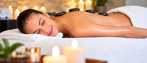A person receiving a hot stone massage with candles and a plant in the background.