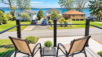 Una terraza con dos sillas y una mesa, con vista a una calle con casas y un cuerpo de agua.