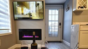 Un salon moderne avec une table basse en verre, une cheminée, un téléviseur et une bouteille de vin.