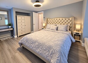 Une chambre à coucher avec un grand lit, une table de chevet, une commode, une armoire et un miroir.