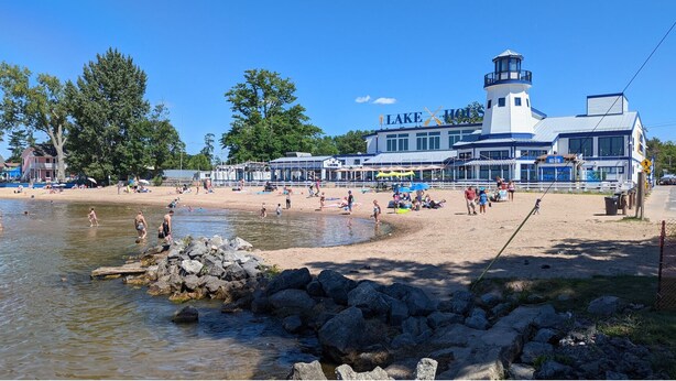 Un hôtel situé au bord d’un lac, doté d’un quai, d’une plage et d’un grand bâtiment surmonté d’une tour.