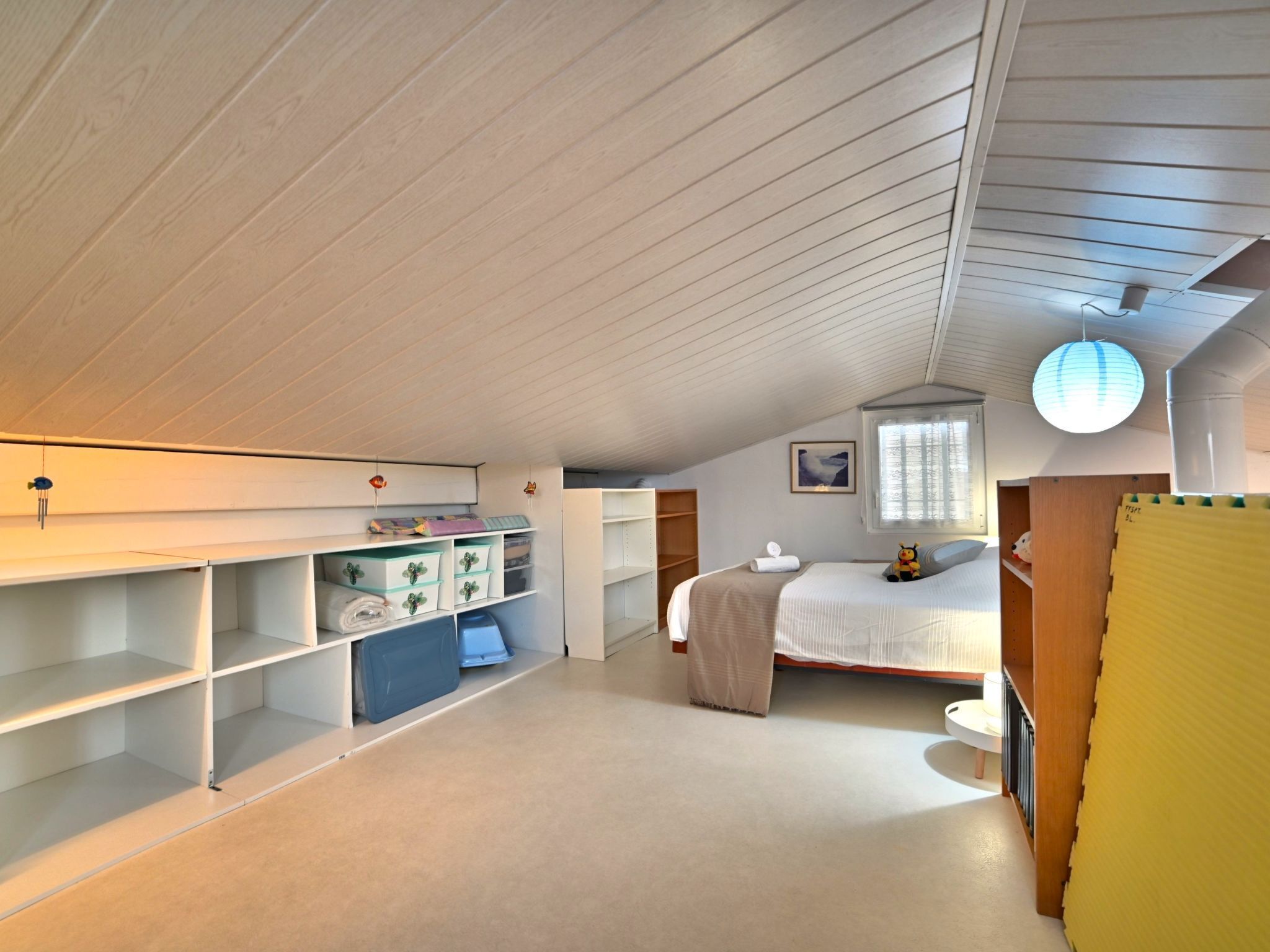 A spacious attic bedroom with a sloped ceiling, built-in shelving, a bed, and a window.