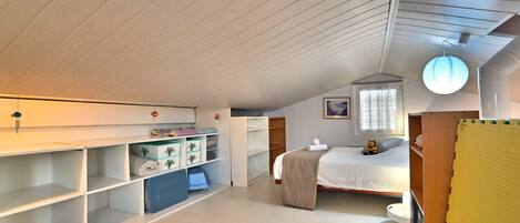 A spacious attic bedroom with a sloped ceiling, built-in shelving, a bed, and a window.