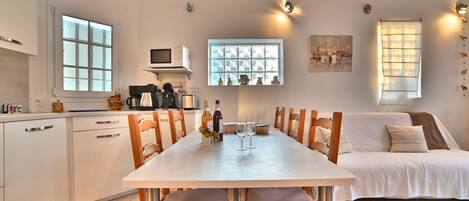 A modern kitchen with white cabinets, a dining table, and chairs. There is a microwave, coffee maker, and a window with a view.