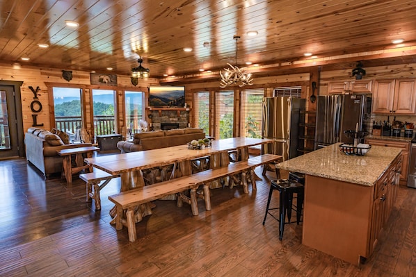 L’intérieur d’un chalet en bois comprend une grande table à manger, des bancs en bois, un coin cuisine et une cheminée.