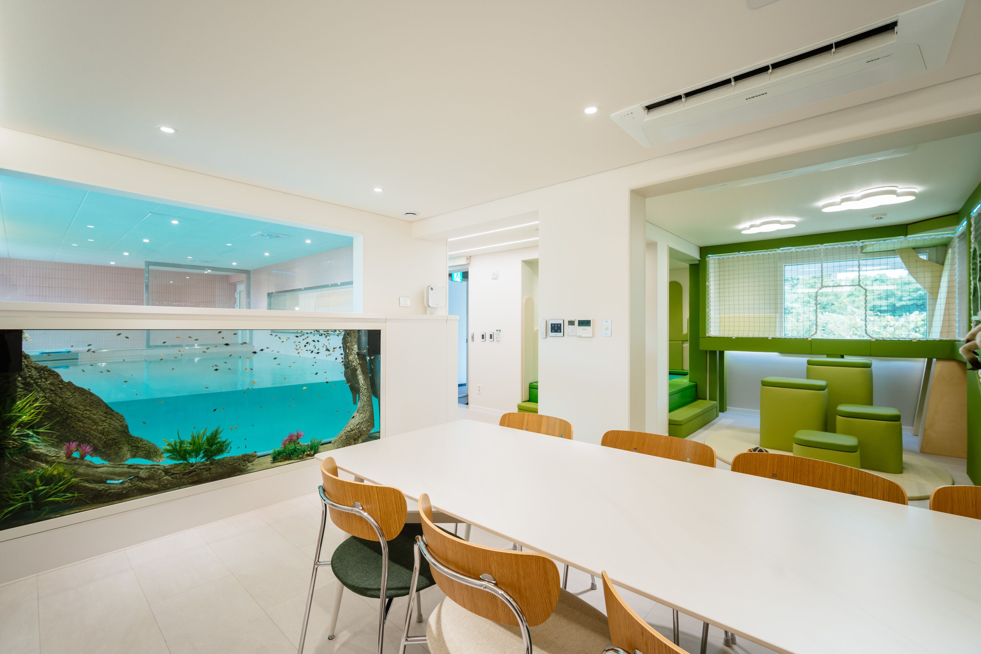Una sala de conferencias moderna con una larga mesa, sillas de madera y un gran acuario con paisaje rocoso y peces.