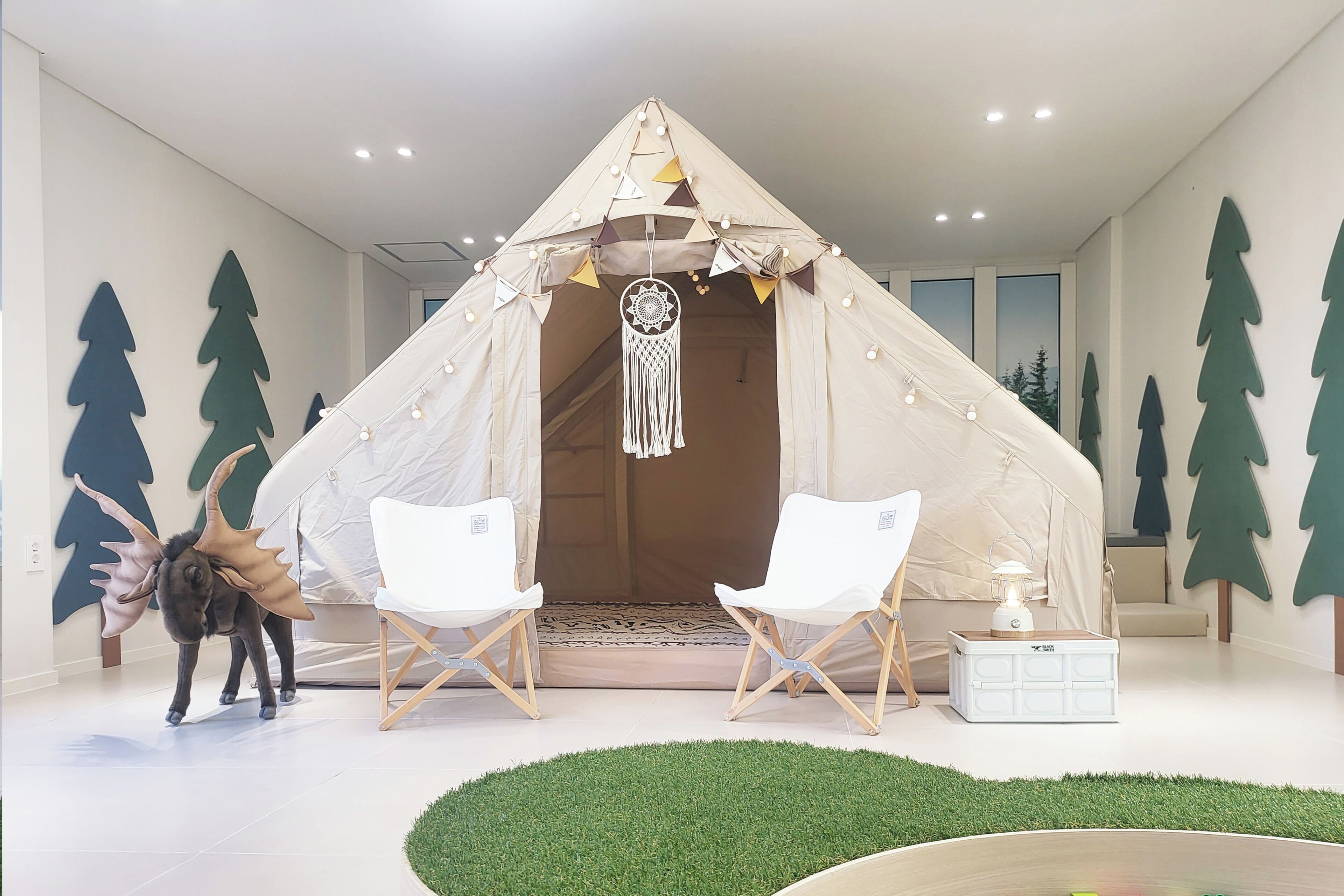 A tent-like structure with a dreamcatcher, two white chairs, and a small table with a lantern.