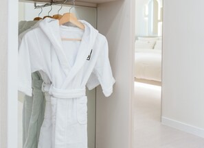 A white robe hanging on a wooden hanger in a closet with a mirror reflecting a bed in the background. - Pico Kids Pool Villa (Busan)