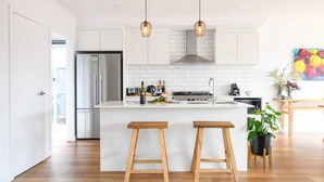 Una cocina moderna con armarios blancos, un refrigerador de acero inoxidable, una isla central con taburetes, iluminación colgante y un cuadro en la pared.