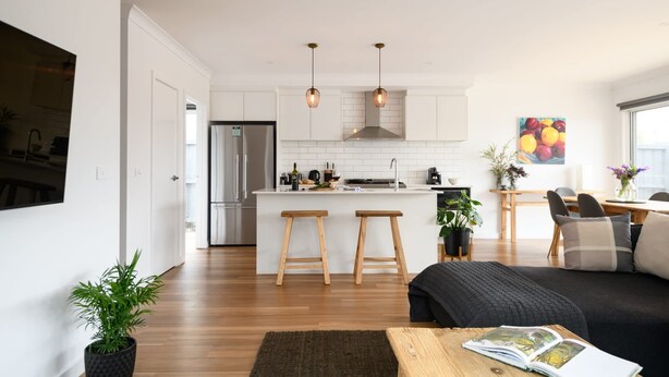 Una cocina moderna con armarios blancos, un refrigerador de acero inoxidable, taburetes de madera e iluminación colgante.