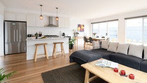 Una cocina moderna con un refrigerador de acero inoxidable, taburetes de madera y una zona de comedor con un sofá negro y una mesa de centro.