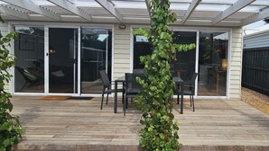 Un patio cubierto con piso de madera, puertas correderas de vidrio y una disposición de mesa y silla negra.