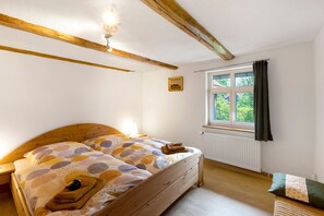 Une chambre avec un lit en bois, une fenêtre avec des rideaux, un radiateur et un petit tableau accroché au mur.