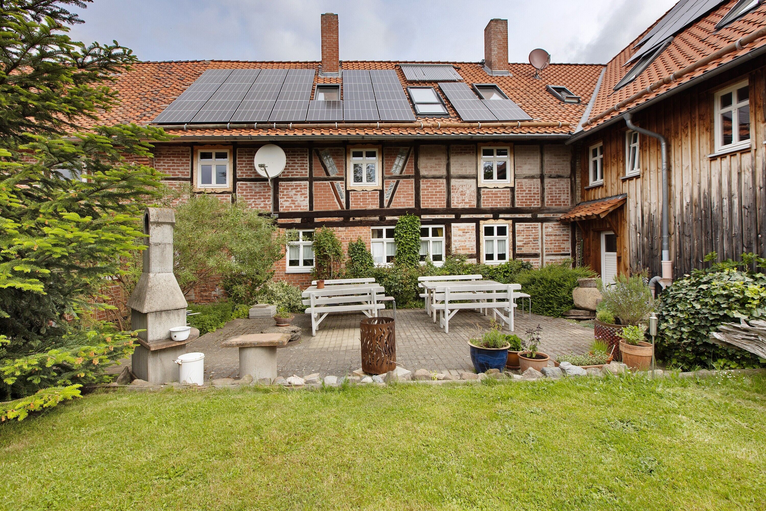 Ein traditionelles Fachwerkhäuschen mit Solaranlage, Sitzgelegenheit im Freien und einem Garten.