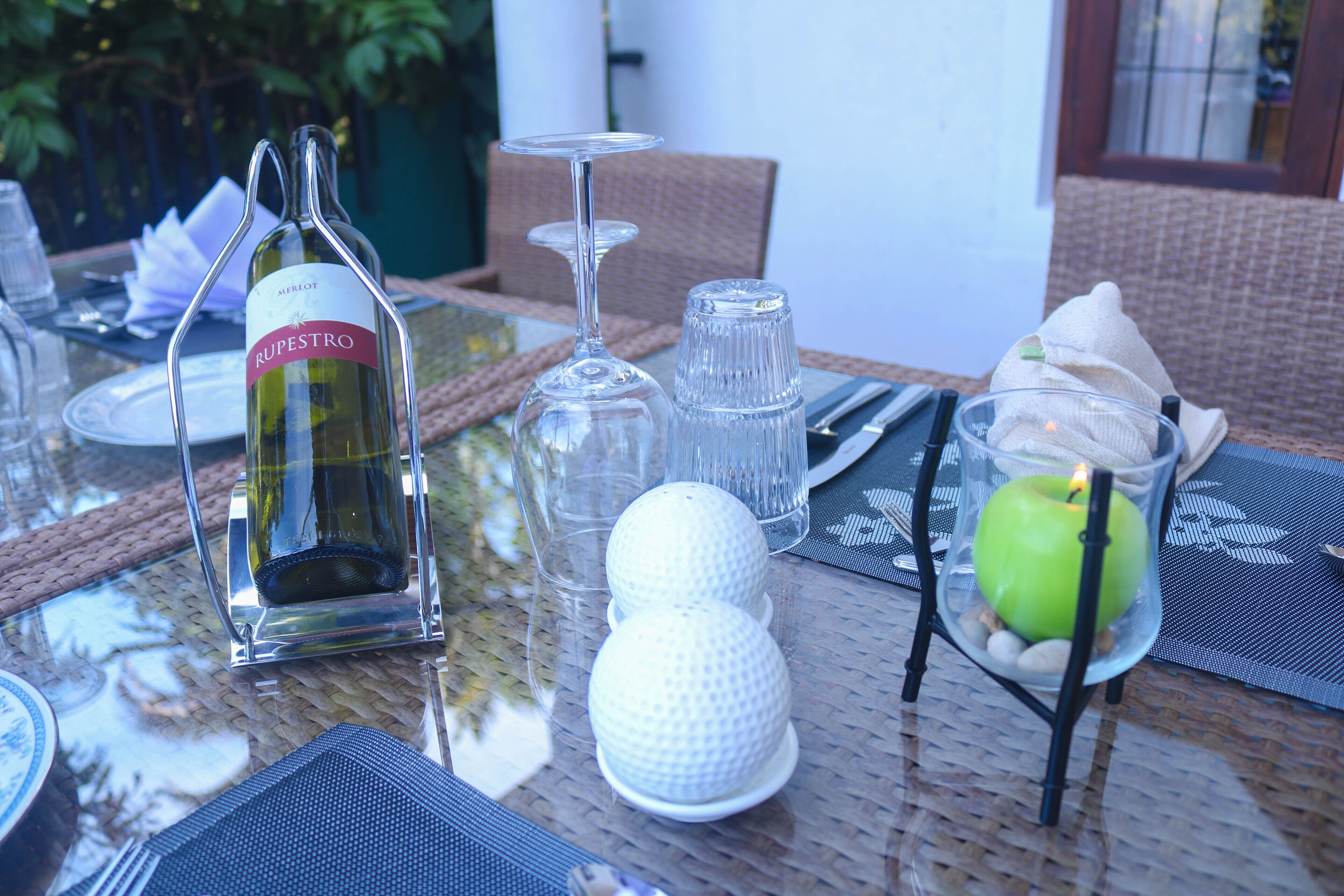 Une table à manger dressée avec une bouteille de vin, des verres à vin et un porte-bougie décoratif surmonté d’une pomme.