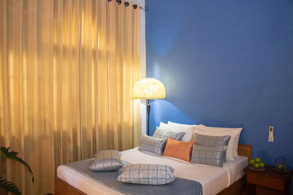 A hotel room with a bed, pillows, a lamp, and a nightstand.