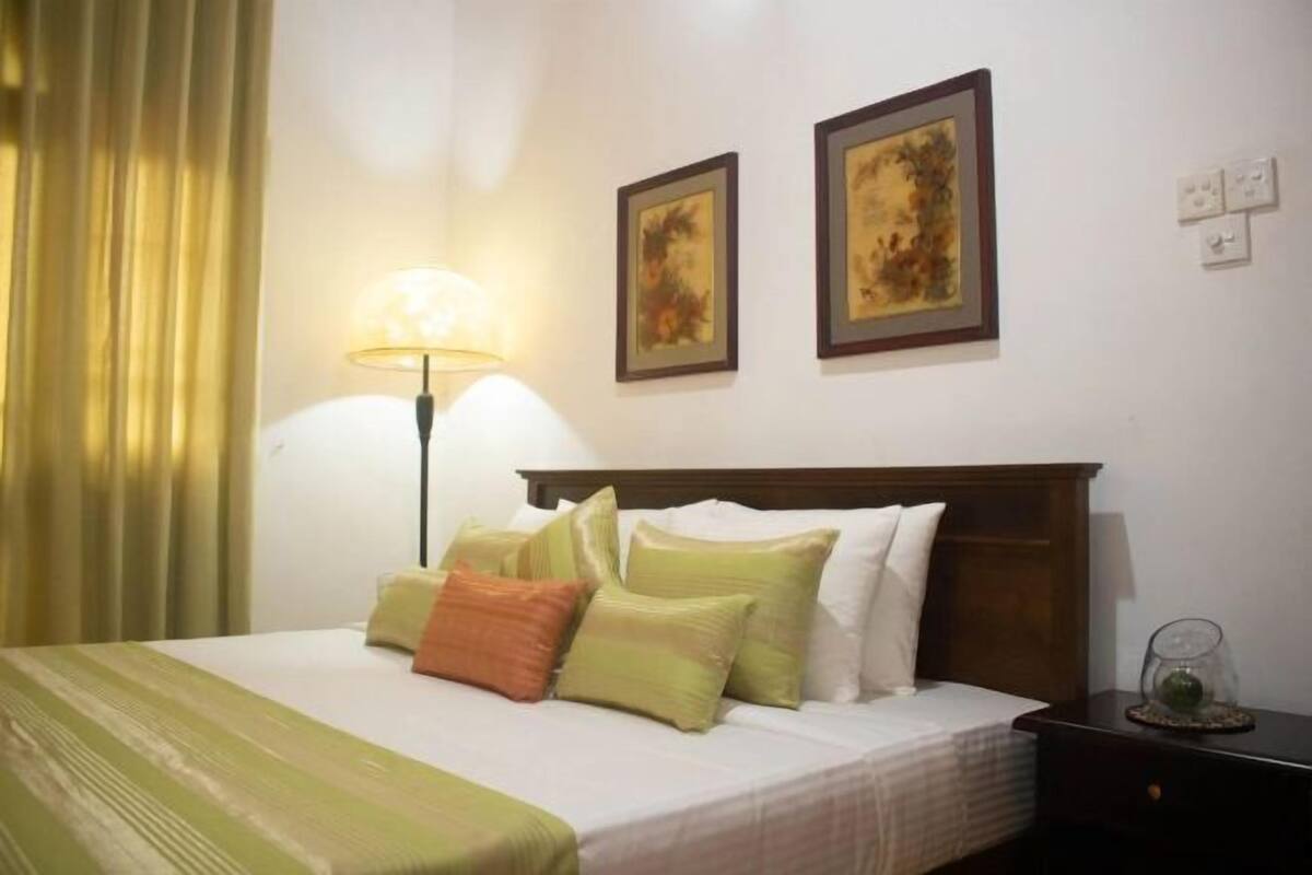A hotel room with a bed, a lamp, and two framed pictures on the wall.