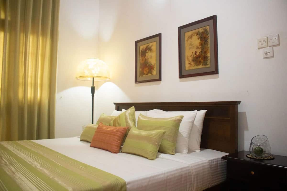 A hotel room with a bed, a nightstand, a lamp, and two framed pictures on the wall.