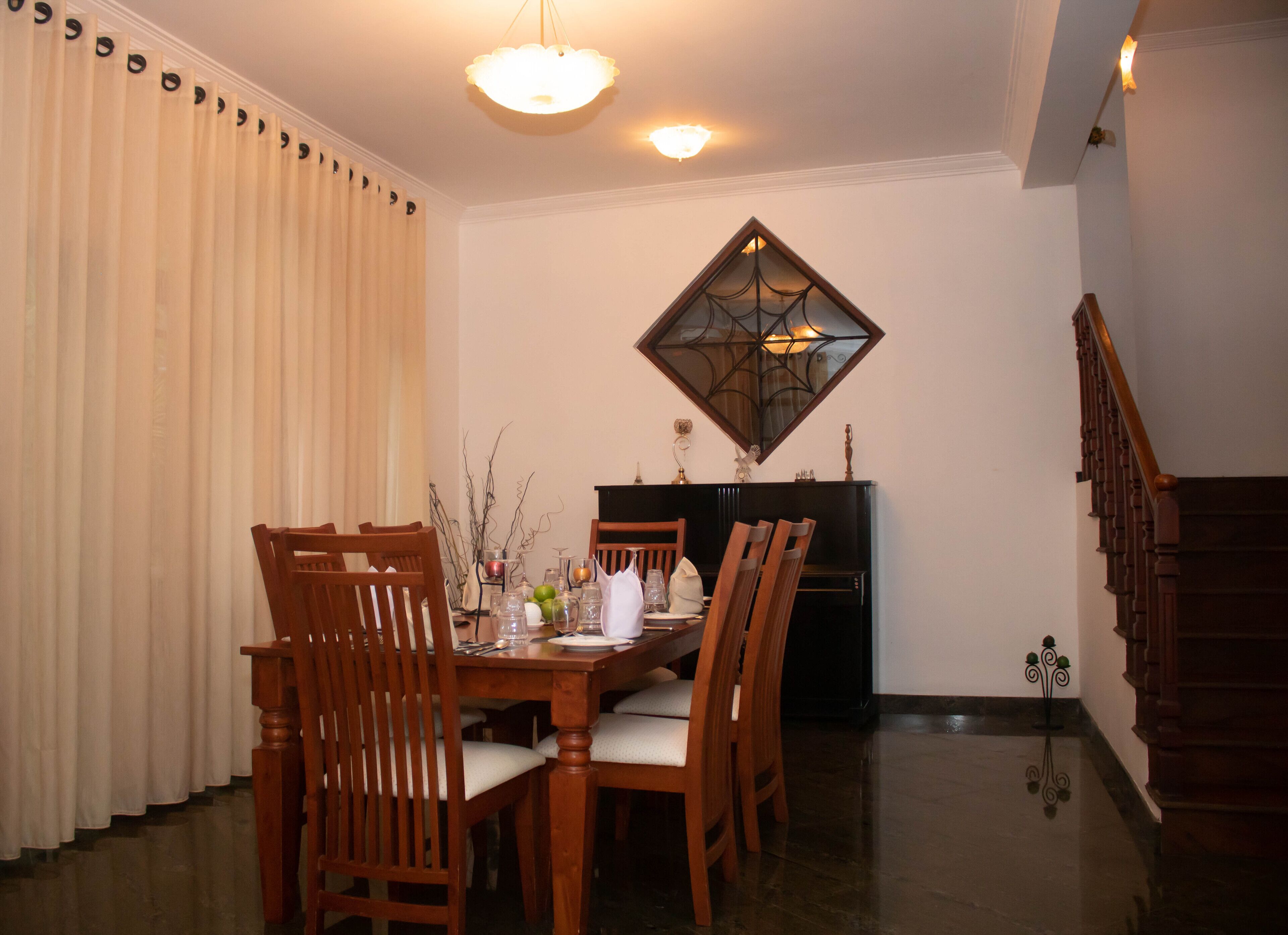 Un coin repas avec une table et des chaises en bois, un lustre et un miroir décoratif au mur.
