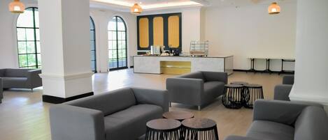 A modern lounge area with grey sofas, round tables, and a central bar area with a white countertop.