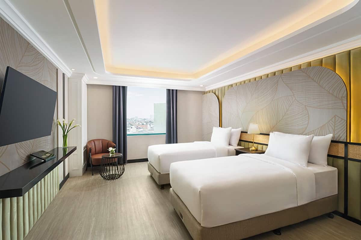 A hotel room with two beds, a TV, a small table with a chair, and a view of the city.