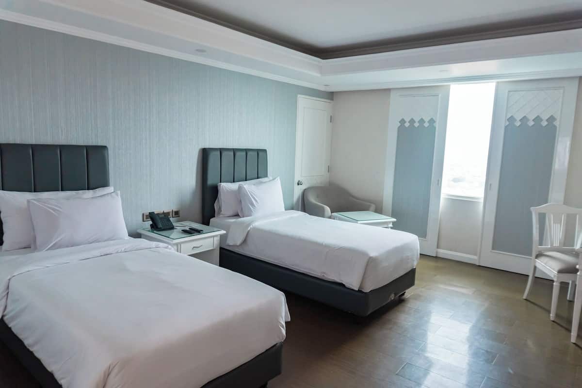 A hotel room with two beds, a desk, a chair, and a large window.