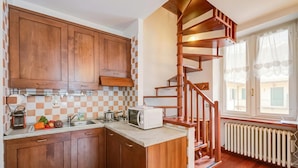 A kitchen with wooden cabinets, a microwave, a sink, and a staircase leading to a balcony.