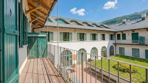 A building with a wooden balcony, green shutters, and a courtyard with a view of a mountain.