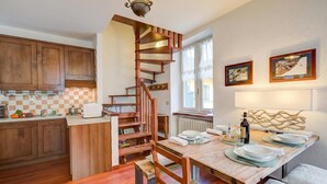 A kitchen with wooden cabinets, a wooden staircase, a dining table set with plates and glasses, and a window with curtains.