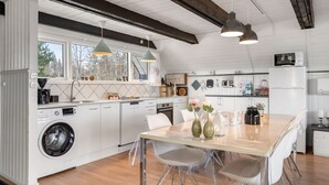 Una cuina moderna amb rentamàquina integrada, zona de menjador amb taula i cadires, i lluminàries penjants.