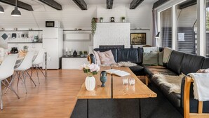 Un saló modern amb una taula baixa de fusta, un sofà de pell negra i una zona de menjador amb cadires blanques.