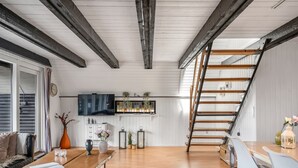 Una habitació àmplia amb una taula de menjador de fusta, un sofà, un televisor fixat a la paret i una escala que condueix a un nivell superior.