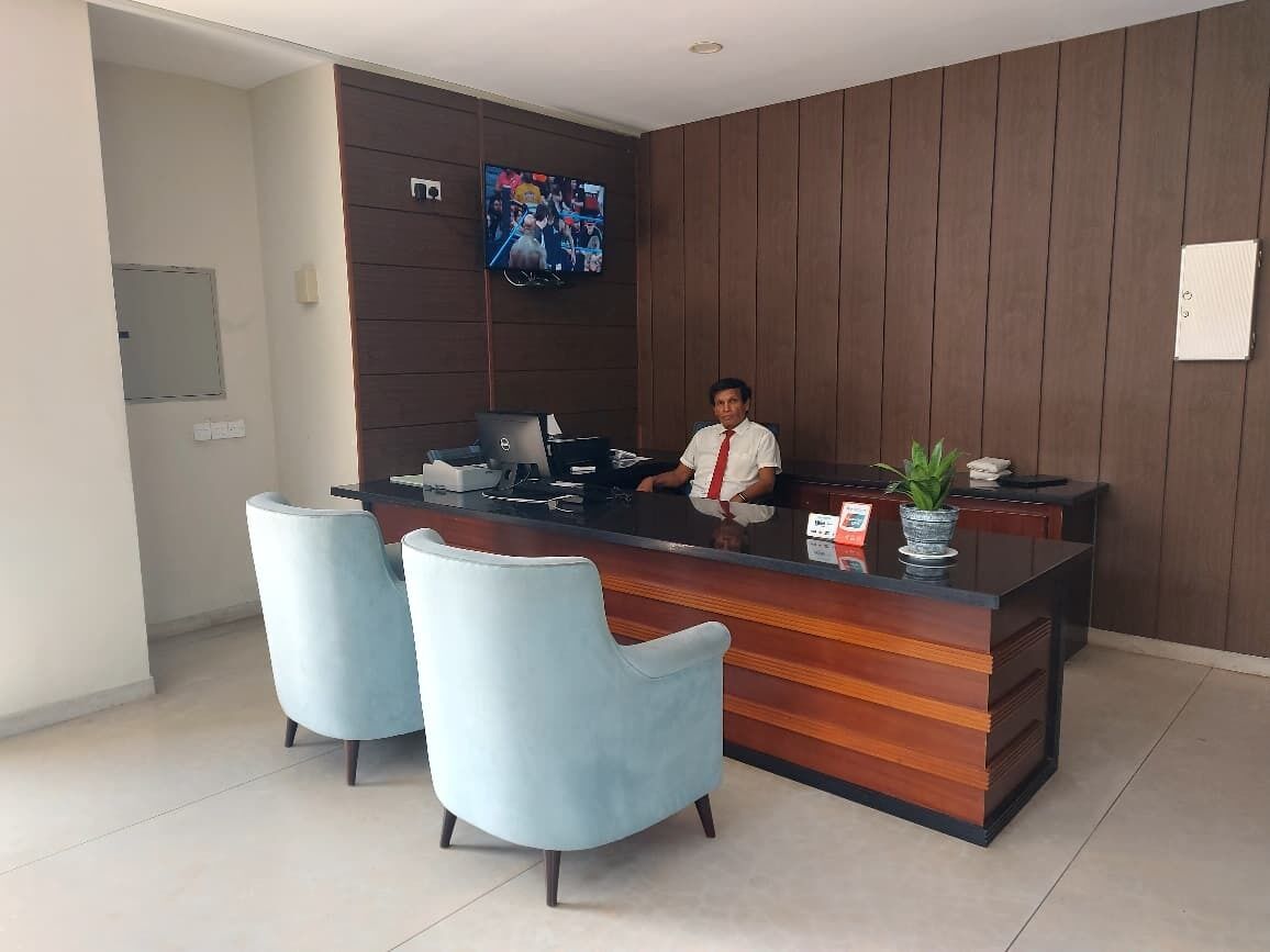 A reception desk with a wooden finish, a flat-screen TV mounted on the wall, and two light blue chairs in front.