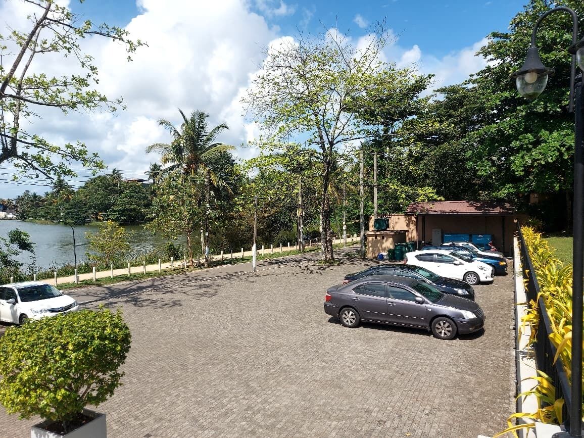 A parking area with several cars, a building with a red roof, and a body of water in the background.