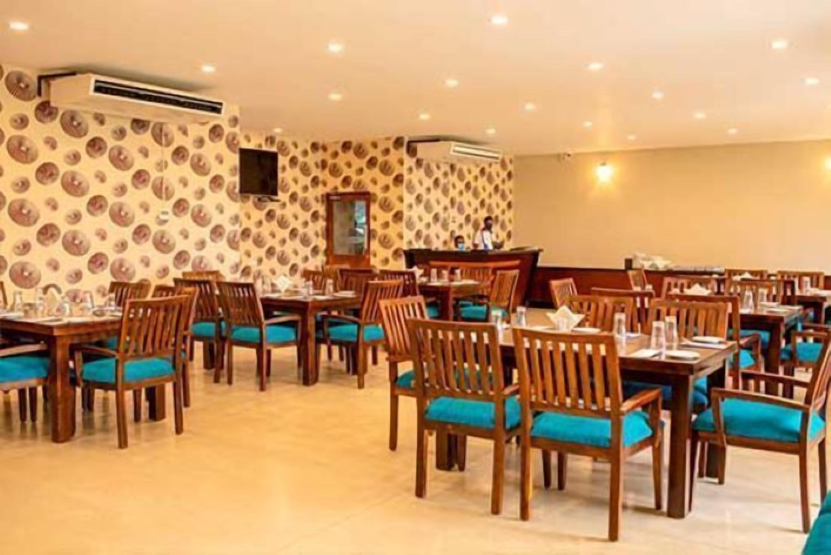 Un restaurant avec des tables et des chaises en bois, un papier peint à motifs et des luminaires au plafond.
