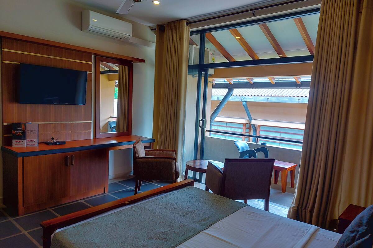 Une chambre d’hôtel avec un lit, un bureau et une chaise, une télévision et une grande fenêtre avec des rideaux.