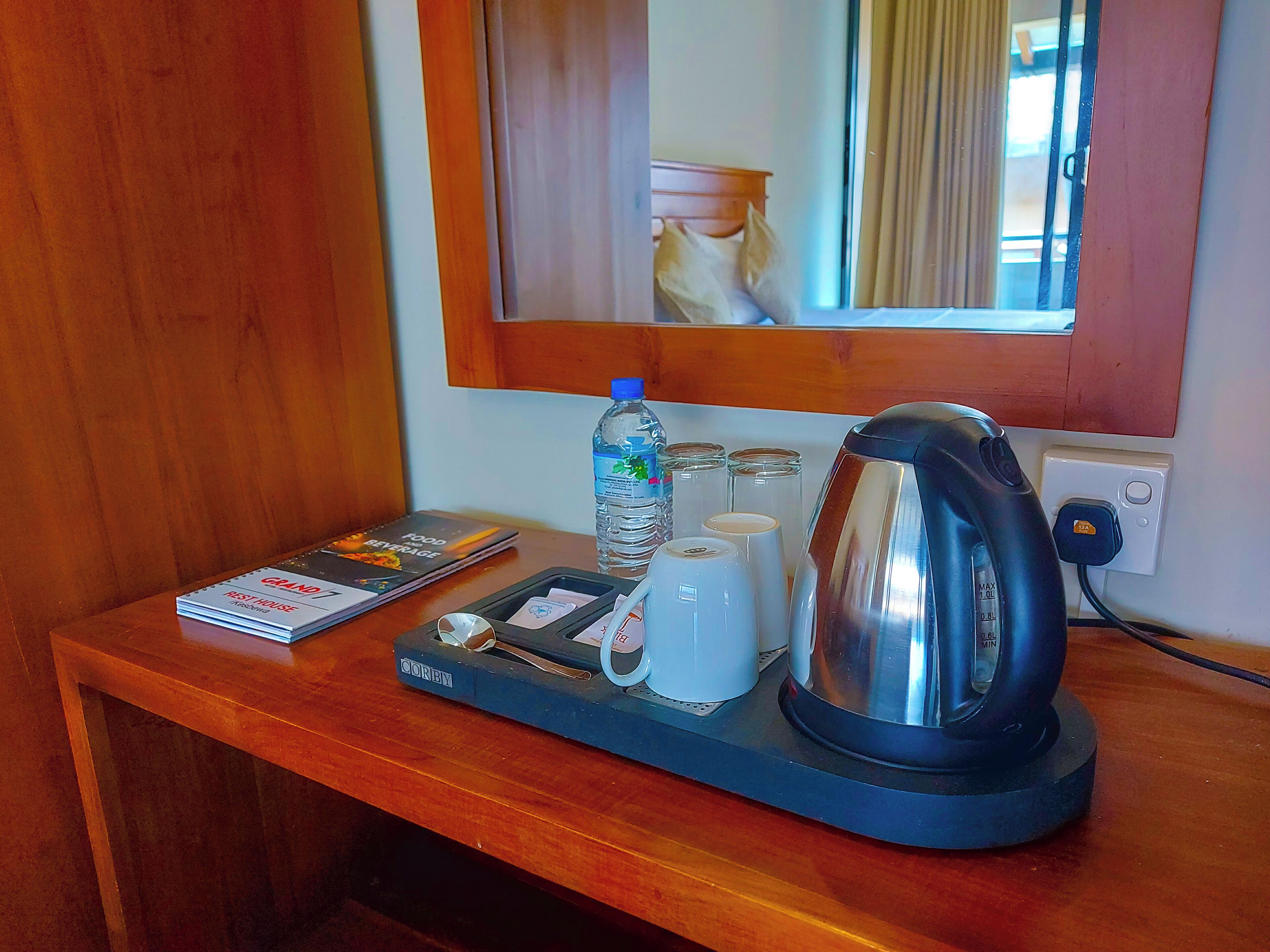 A hotel room's minibar with a water bottle, coffee cups, a kettle, and a menu.