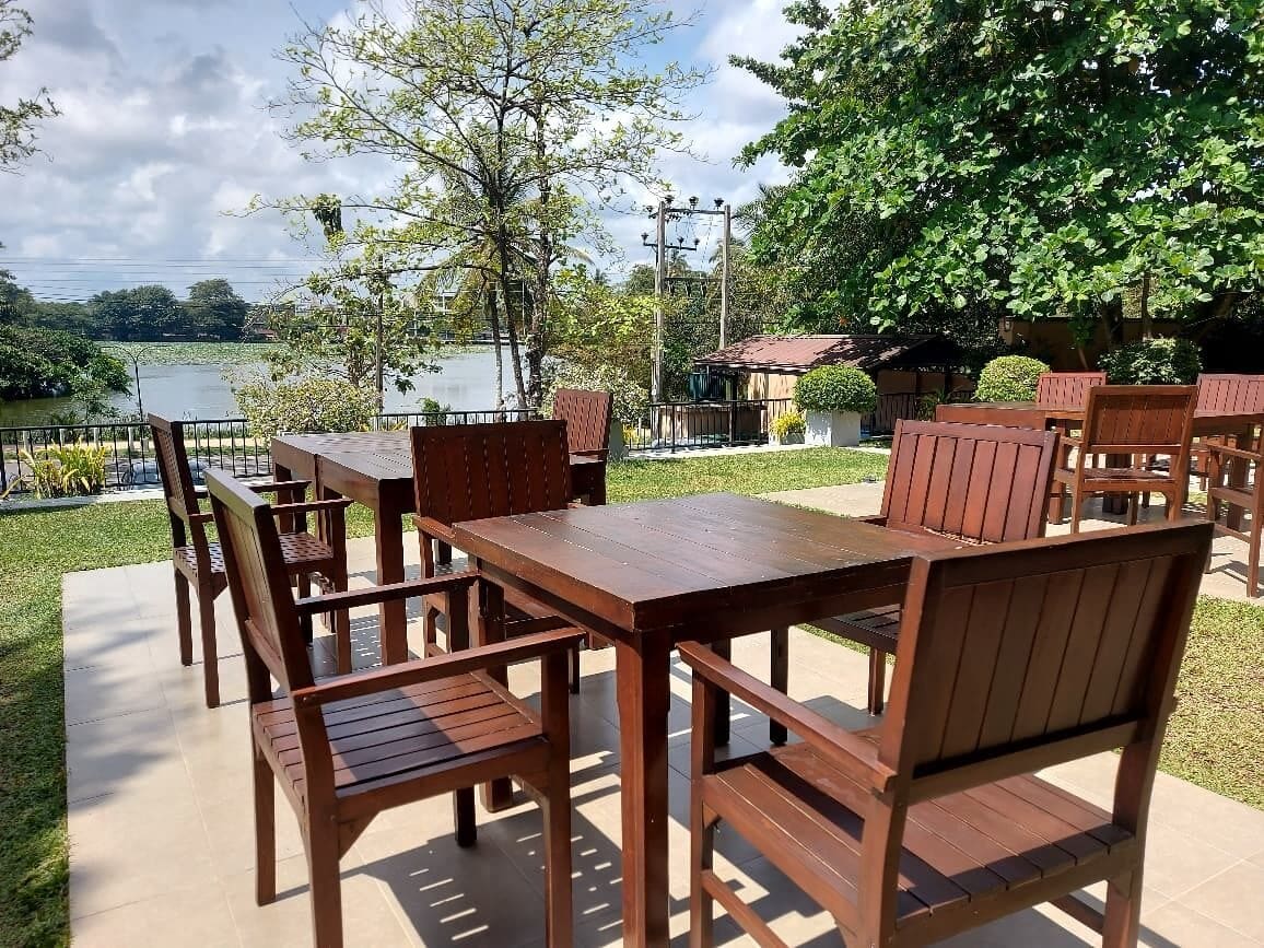 An outdoor patio with wooden furniture, a view of a lake, and a building in the background.